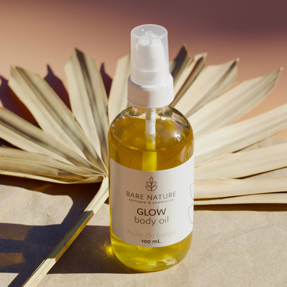 Bottle of Bare Nature Glow body oil with a white label on a brown background with dried leaves.