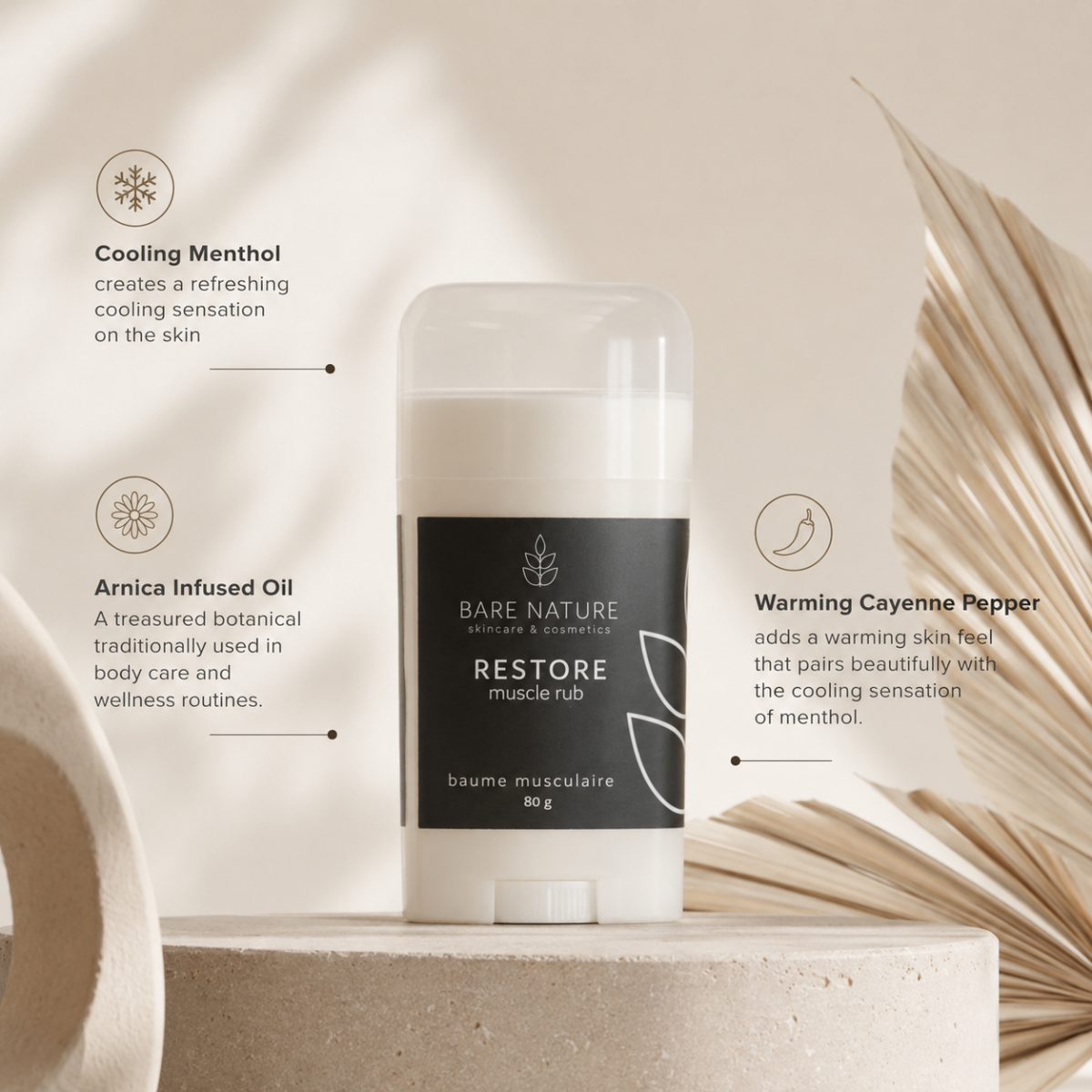 A Bare Nature Restore muscle rub stick container stands on a light stone pedestal, surrounded by decorative dried leaves and text callouts describing cooling menthol, arnica infused oil, and warming cayenne pepper.
