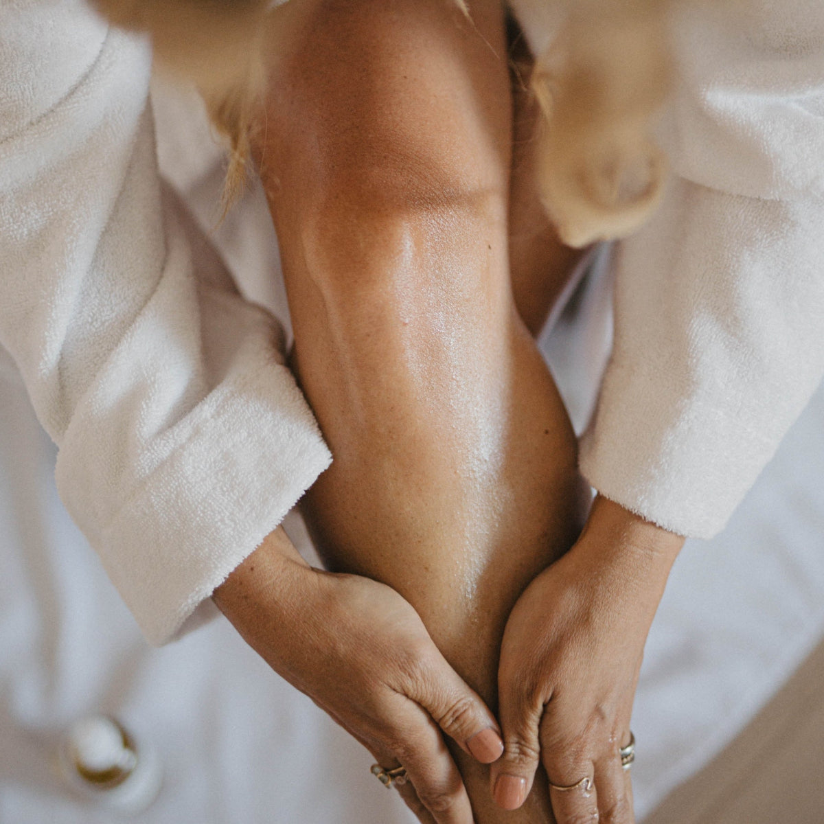 A close-up lifestyle shot of a person applying Bare Nature Restore muscle rub  to their leg while wearing a white bathrobe.