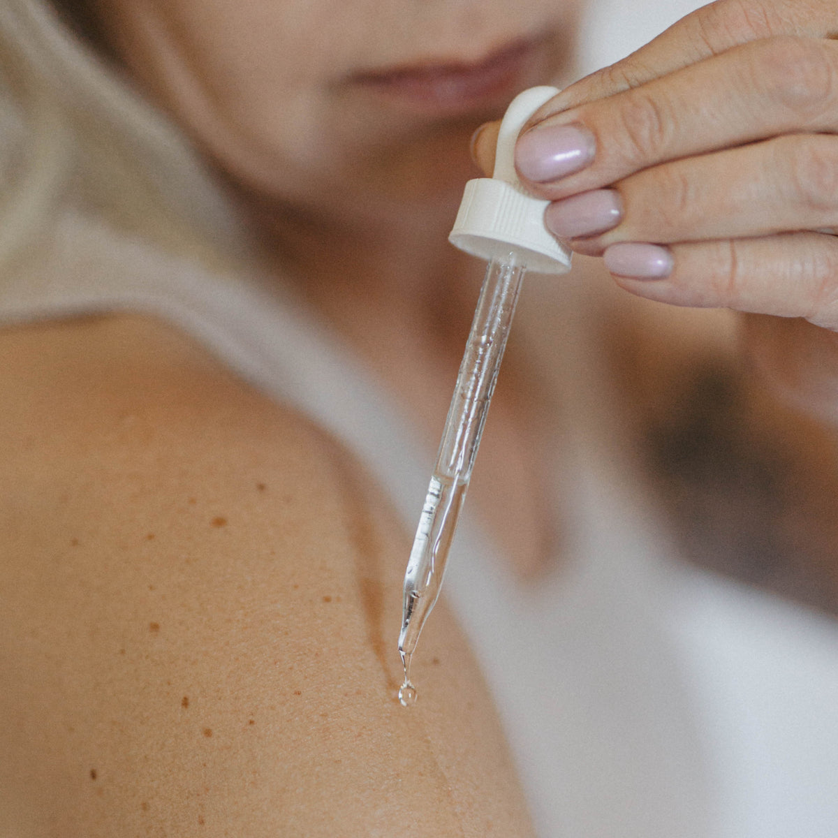 Person applying a dropper of liquid to their skin