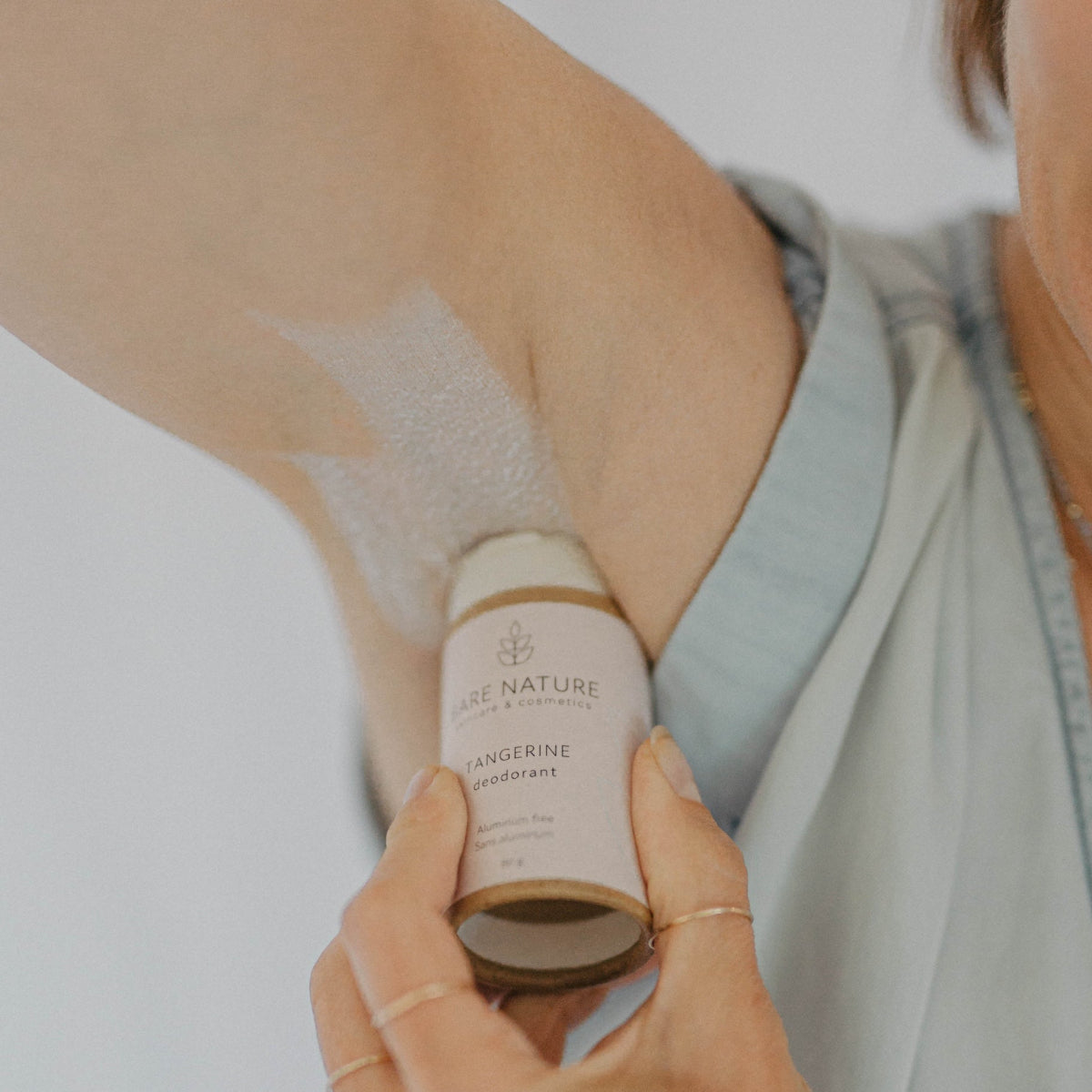 A person applying a stick deodorant to their underarm. Bare Nature Skincare Natural Deodorant in Tangerine Scent