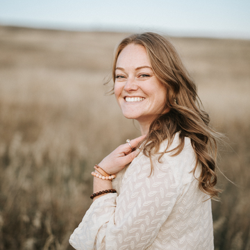 Woman in a beige sweater standing in a field with a blurred background